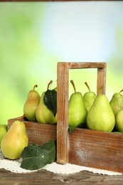 Photo of Crate with fresh pears and leaves on wooden table against blurred green background, closeup