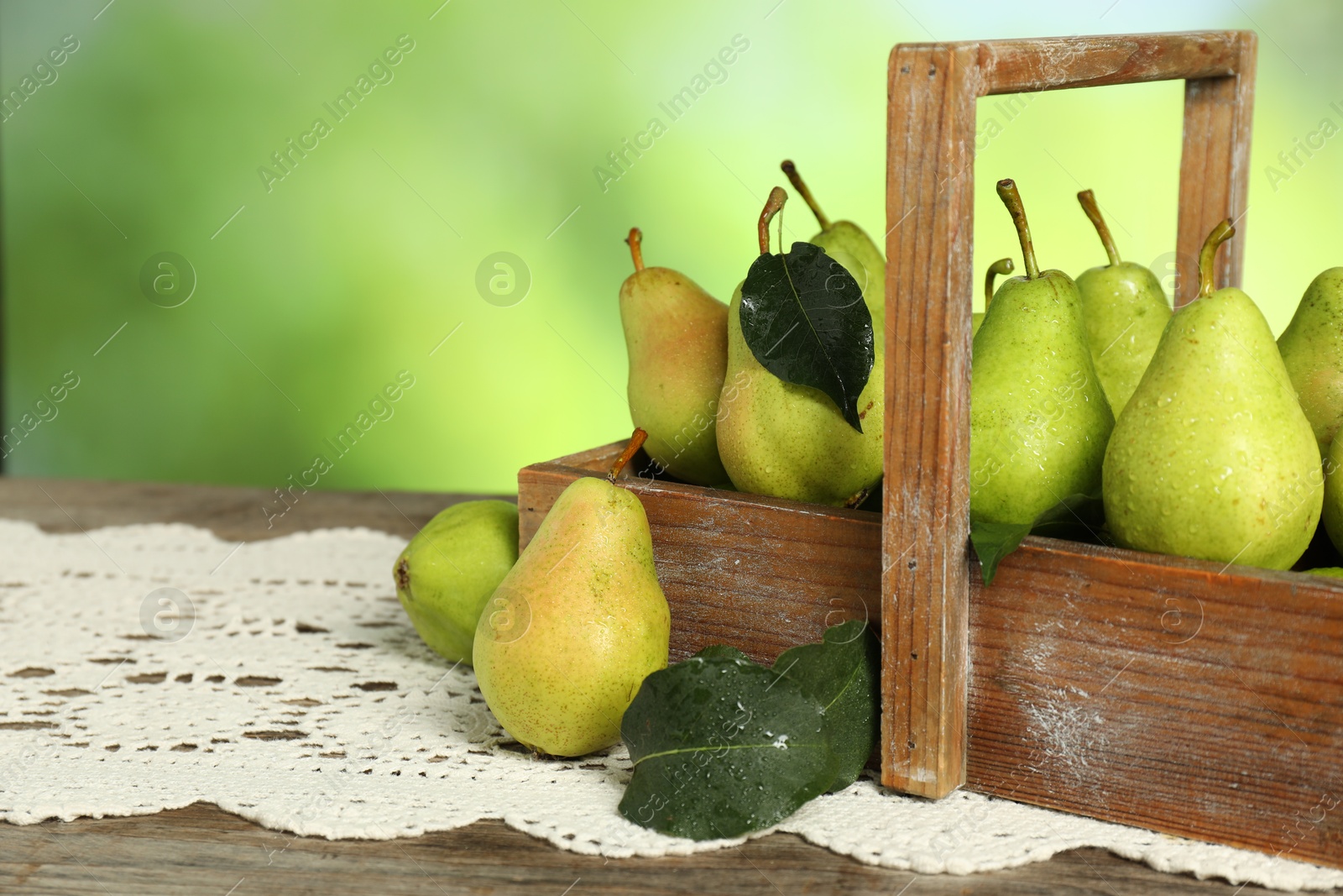 Photo of Crate with fresh pears and leaves on wooden table against blurred green background, closeup. Space for text