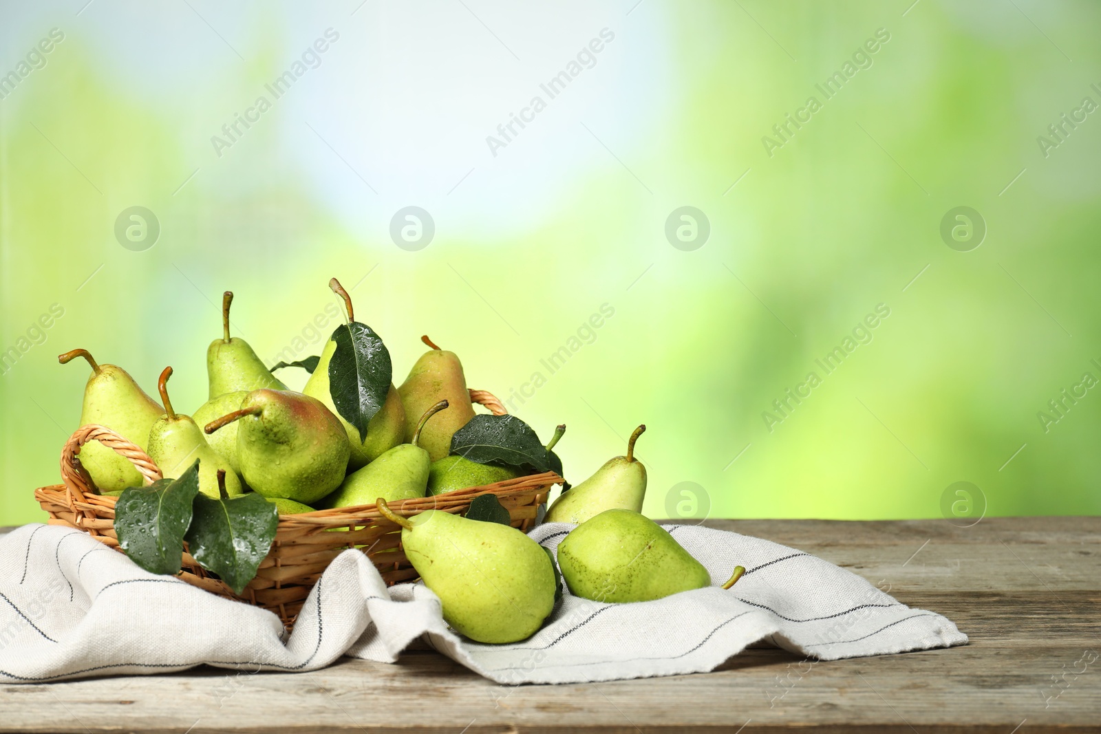 Photo of Fresh pears and leaves with water drops on wooden table against blurred green background. Space for text