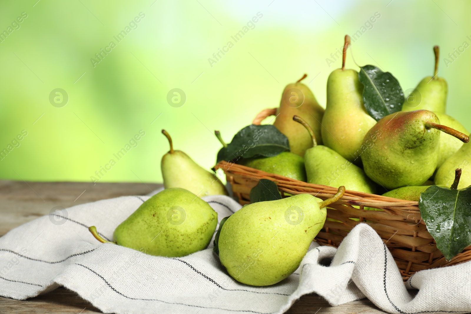 Photo of Fresh pears and leaves with water drops on wooden table against blurred green background, closeup. Space for text