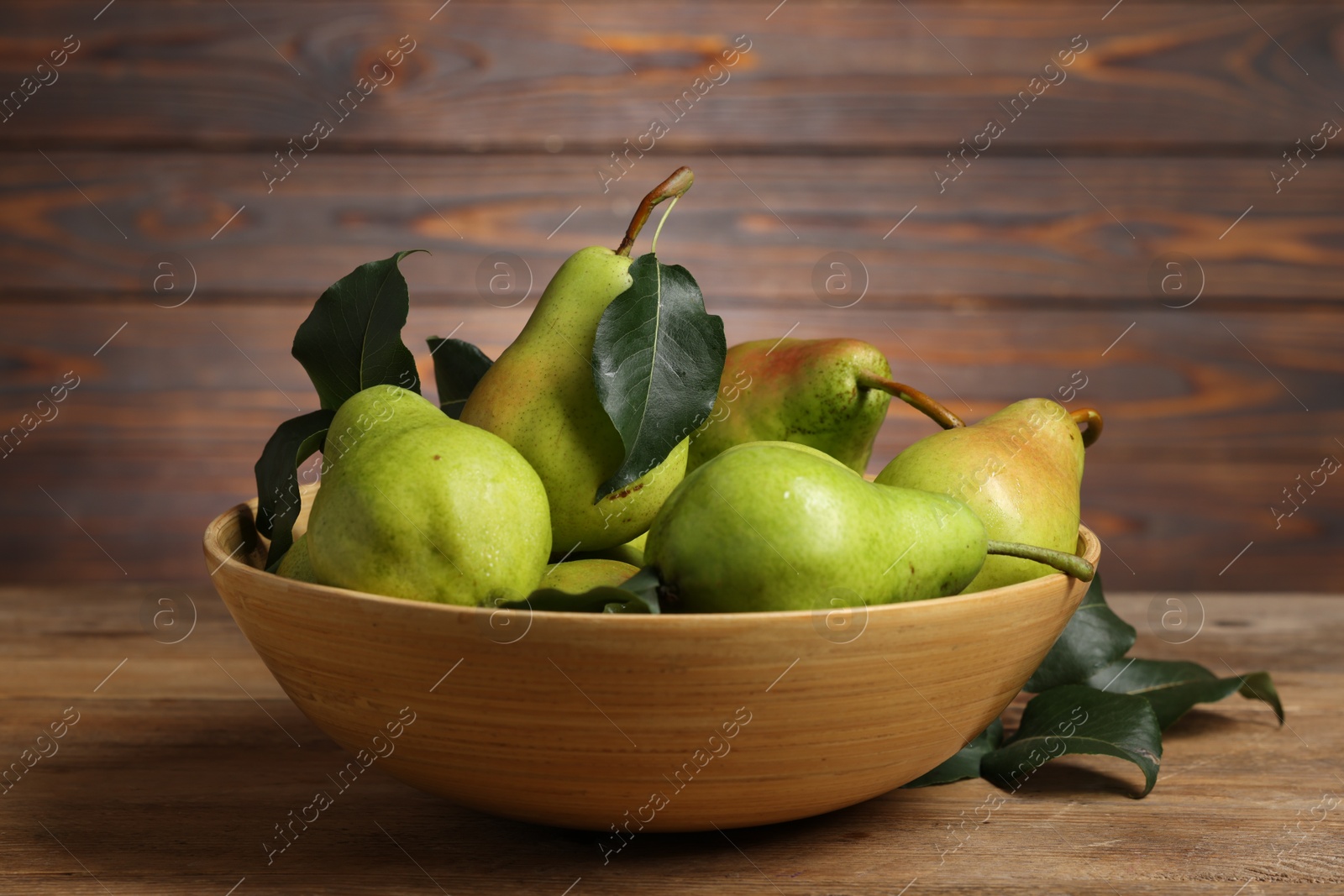 Photo of Fresh green pears and leaves in bowl on wooden table, closeup