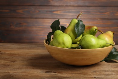 Photo of Fresh green pears and leaves in bowl on wooden table. Space for text