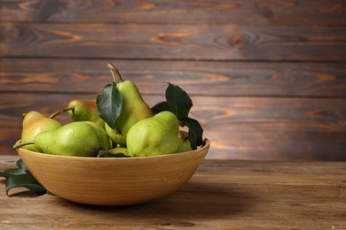 Photo of Fresh green pears and leaves in bowl on wooden table. Space for text