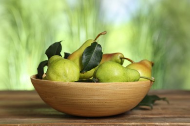 Photo of Fresh pears and leaves in bowl on wooden table against blurred green background, closeup