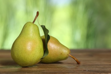 Photo of Fresh pears and leaf on wooden table against blurred green background, closeup. Space for text