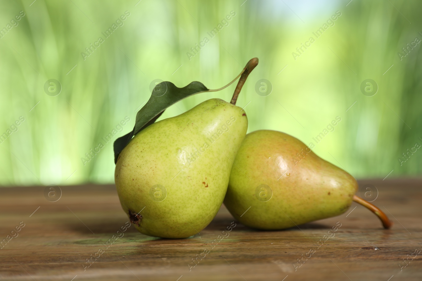 Photo of Fresh pears and leaf on wooden table against blurred green background, closeup