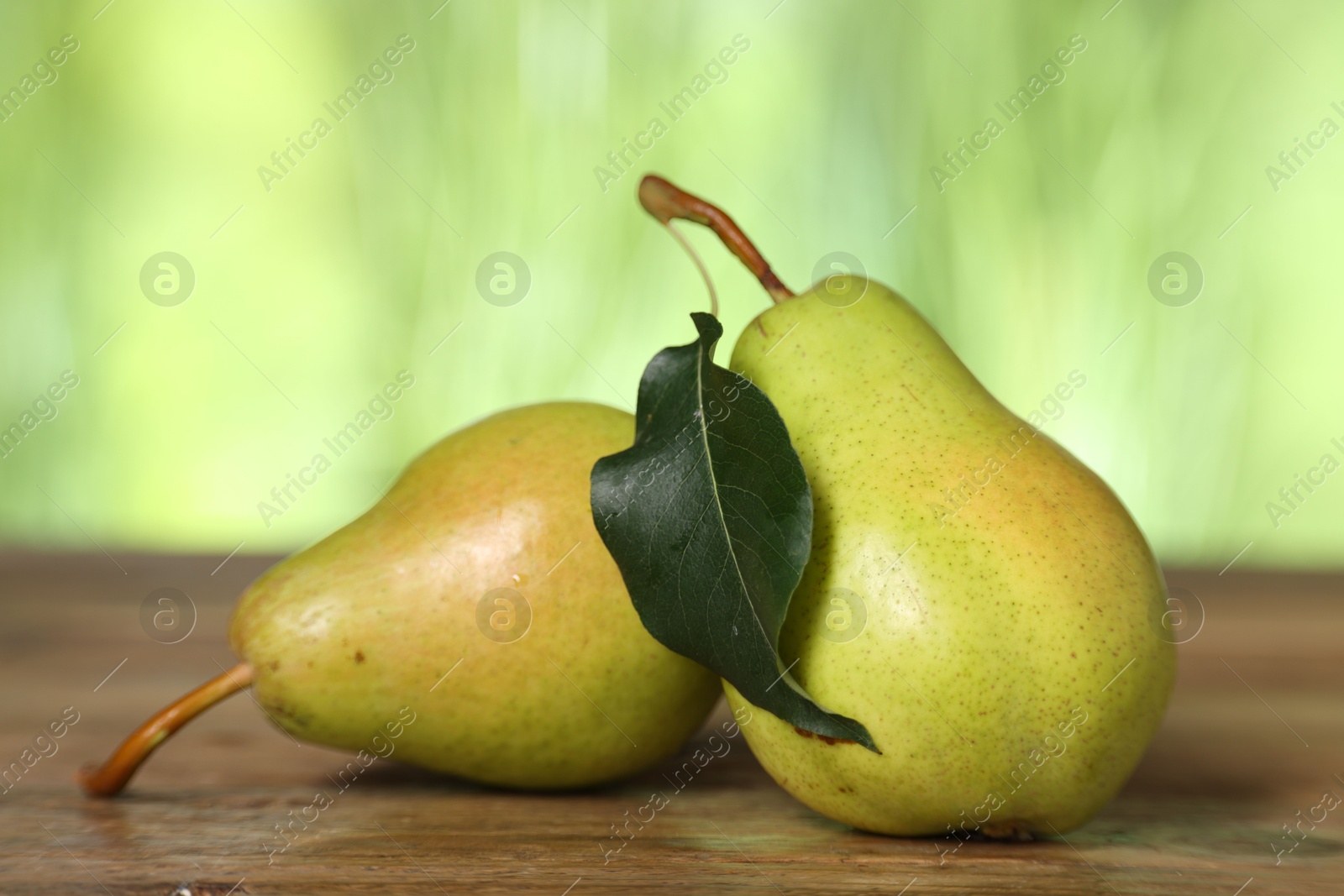 Photo of Fresh pears and leaf on wooden table against blurred green background, closeup