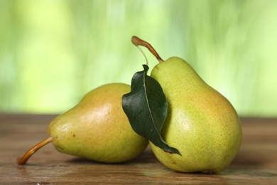 Photo of Fresh pears and leaf on wooden table against blurred green background, closeup