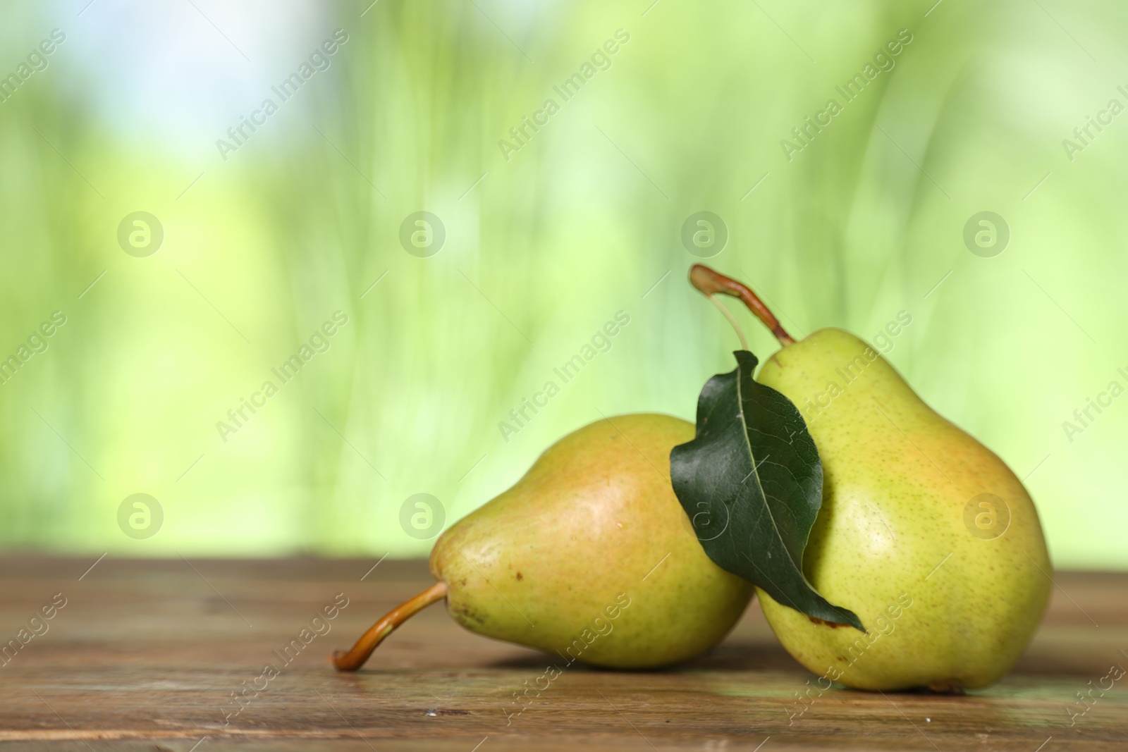 Photo of Fresh pears and leaf on wooden table against blurred green background. Space for text