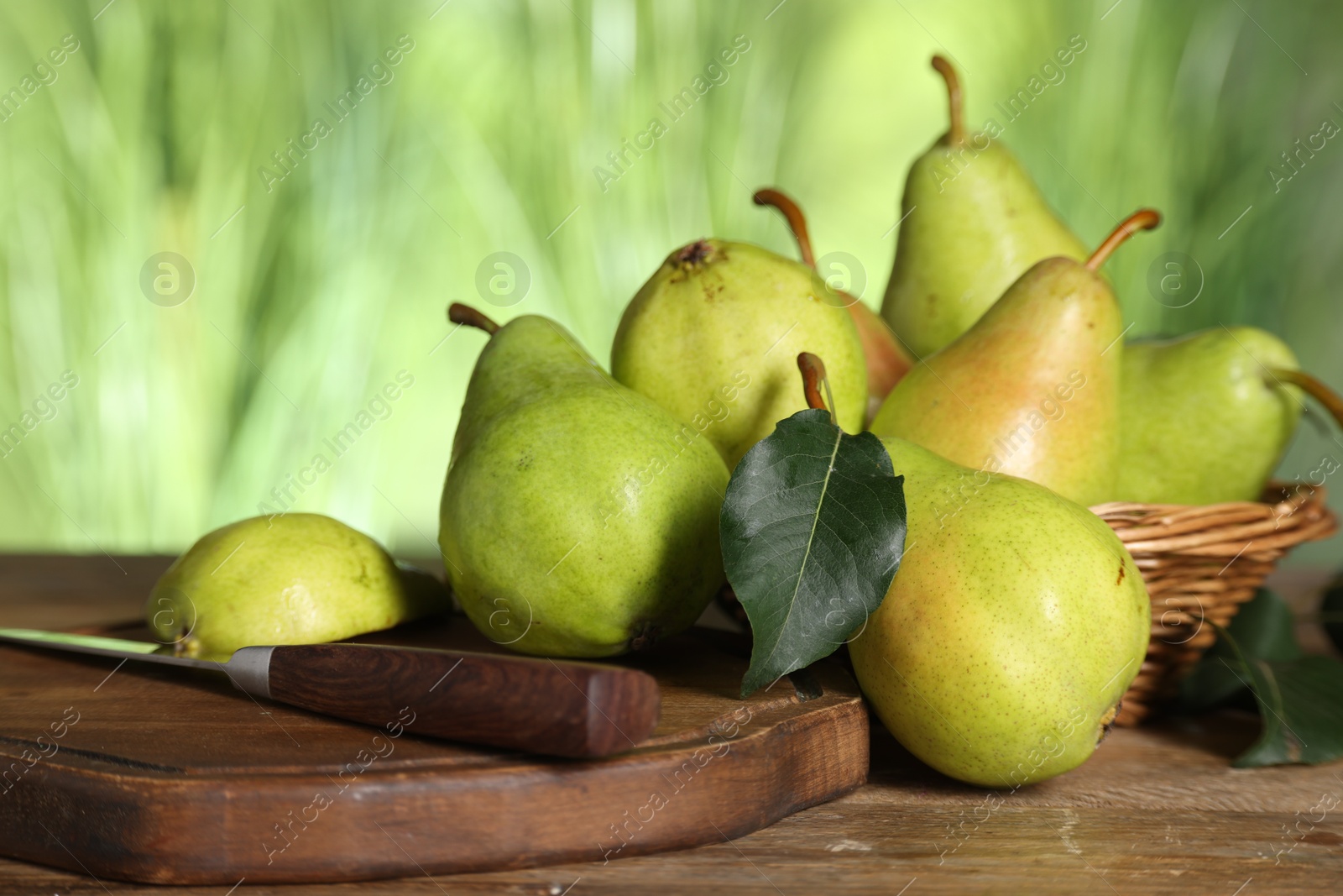 Photo of Fresh pears and leaves on wooden table against blurred green background