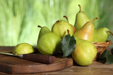 Photo of Fresh pears and leaves on wooden table against blurred green background