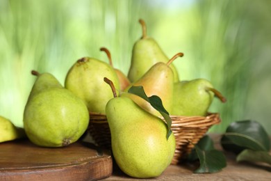 Photo of Fresh pears and leaves on wooden table against blurred green background, closeup