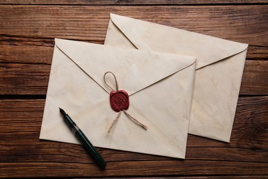 Photo of Old letter envelopes and pen on wooden table, top view