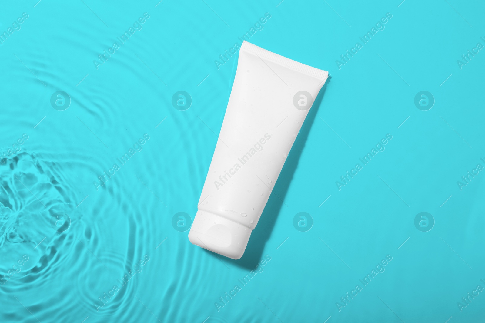 Photo of Cosmetic product. Tube with cream in water on light background, top view