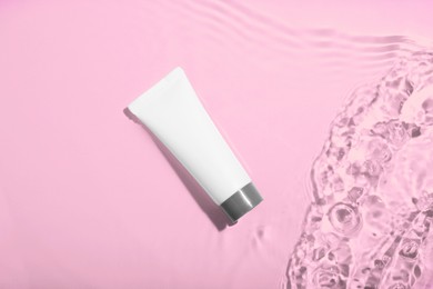 Cosmetic product. Tube with cream in water on light background, top view