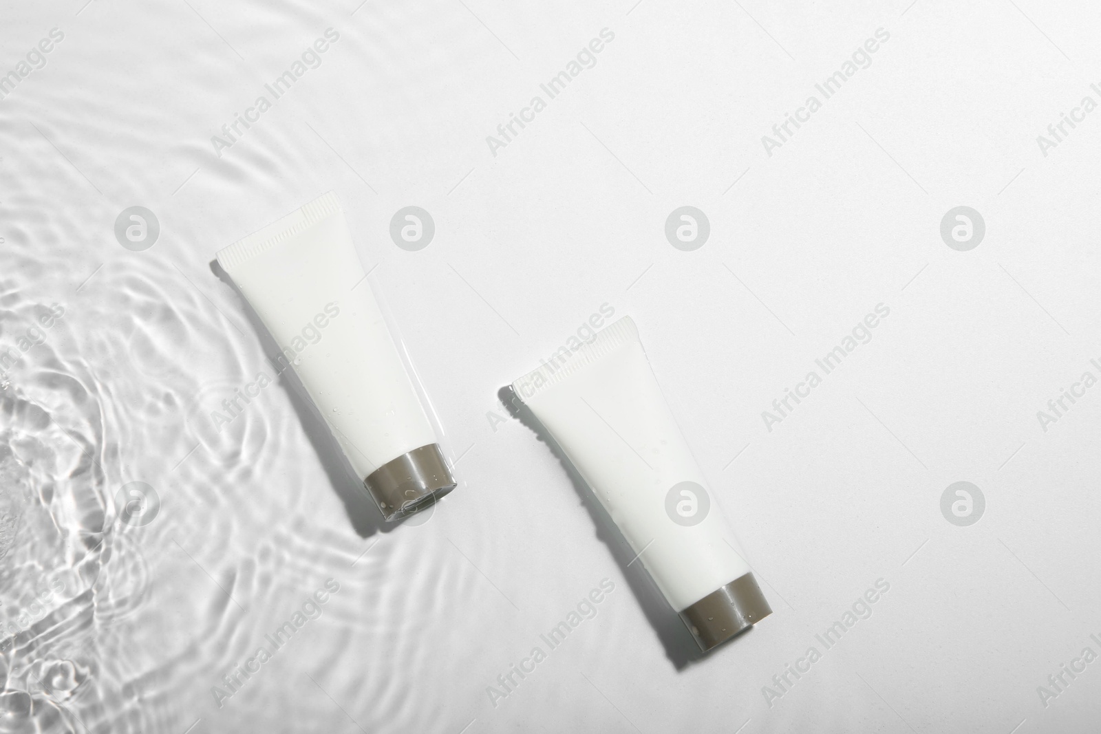 Photo of Cosmetic products. Tubes with cream in water on light background, top view