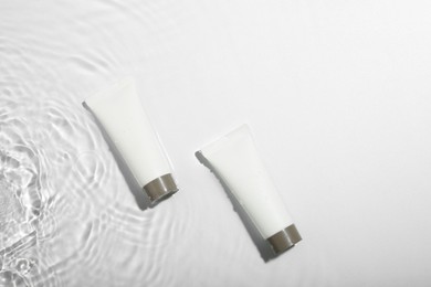 Cosmetic products. Tubes with cream in water on light background, top view