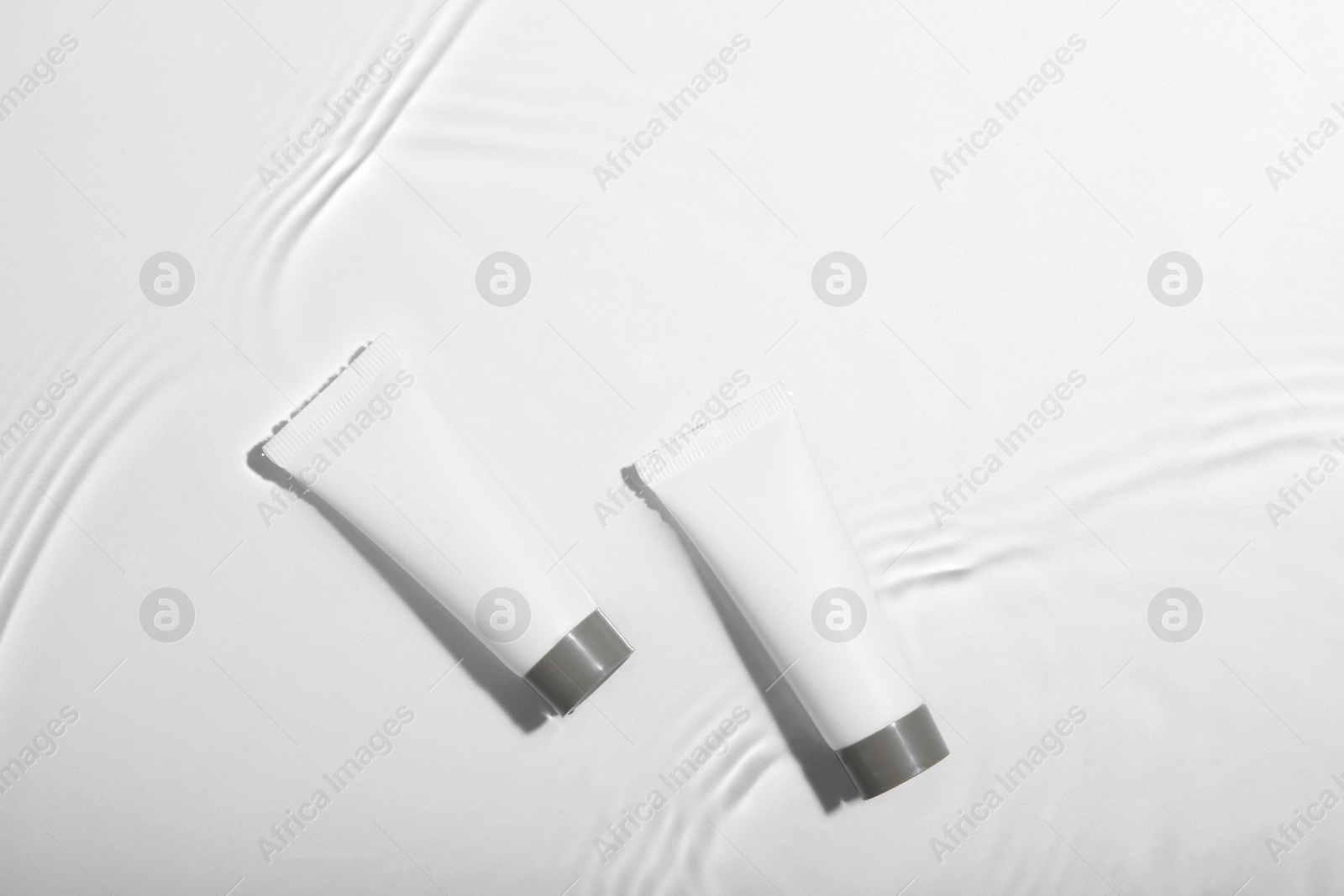 Photo of Cosmetic products. Tubes with cream in water on light background, top view