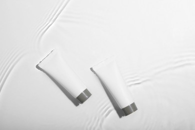 Photo of Cosmetic products. Tubes with cream in water on light background, top view