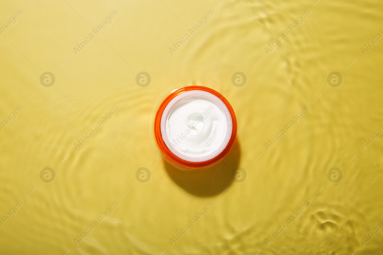 Photo of Jar with cream in water on yellow background, top view. Cosmetic product