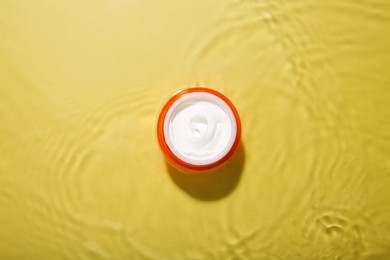 Jar with cream in water on yellow background, top view. Cosmetic product