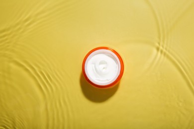 Photo of Jar with cream in water on yellow background, top view. Cosmetic product