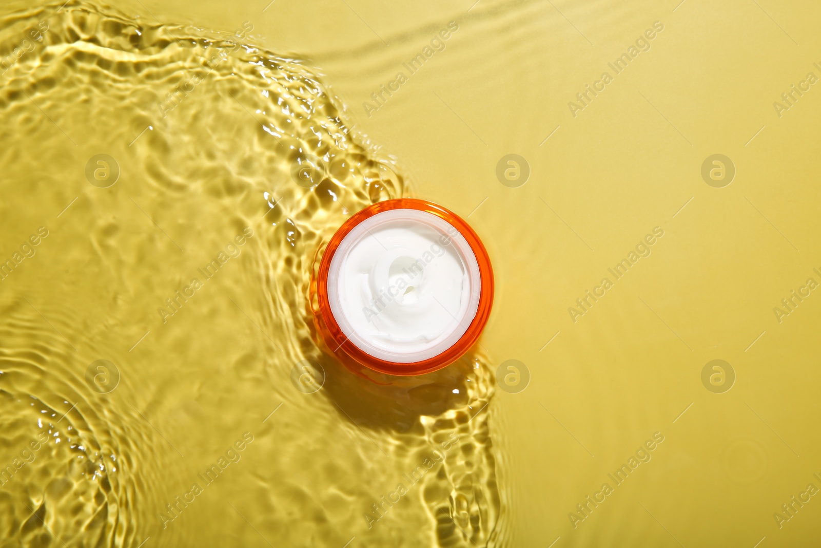 Photo of Jar with cream in water on yellow background, top view. Cosmetic product