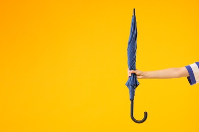 Woman with blue umbrella on yellow background, closeup. Space for text