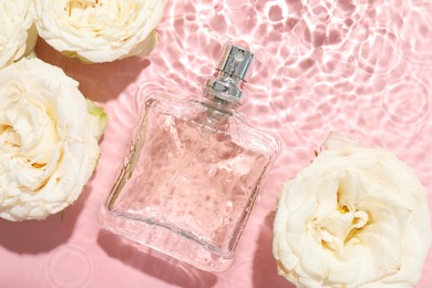 Photo of Beautiful rose flowers and perfume bottle in water on pink background, flat lay