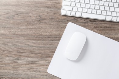 Photo of Computer mouse with mousepad and keyboard on wooden desk, top view. Space for text