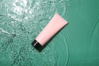 Photo of Cosmetic product. Tube with cream in water on green background, top view