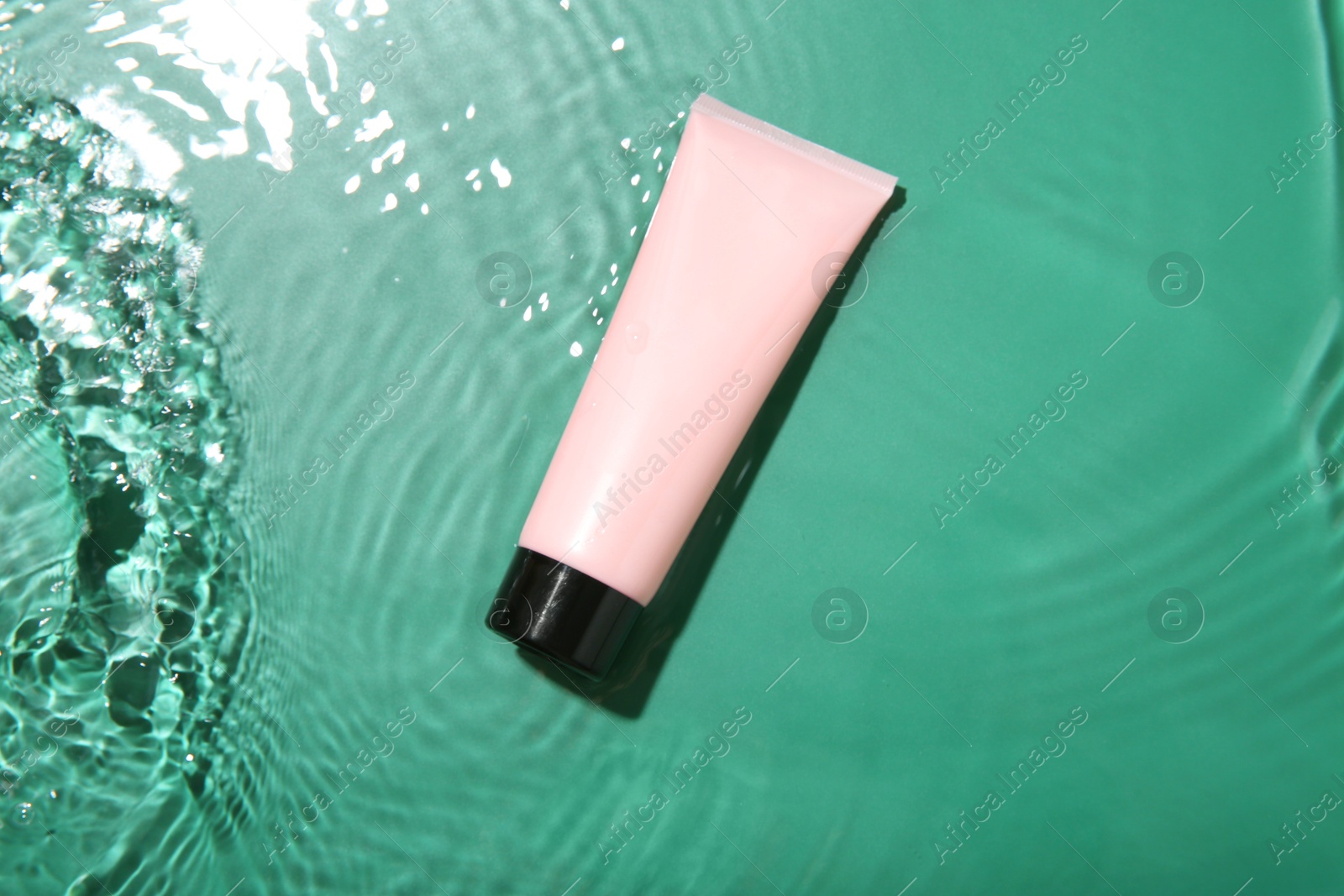 Photo of Cosmetic product. Tube with cream in water on green background, top view