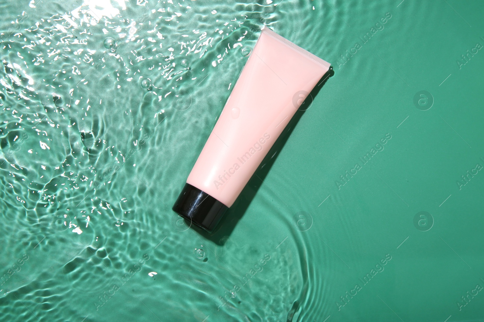 Photo of Cosmetic product. Tube with cream in water on green background, top view