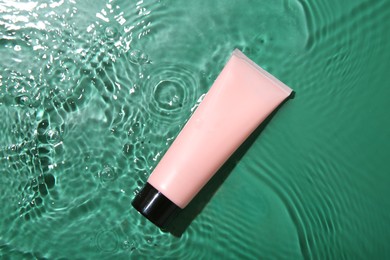 Cosmetic product. Tube with cream in water on green background, top view