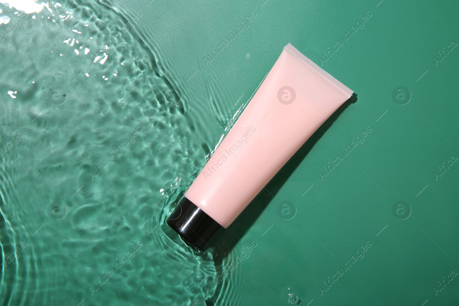 Photo of Cosmetic product. Tube with cream in water on green background, top view