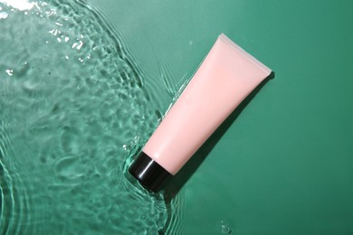 Cosmetic product. Tube with cream in water on green background, top view