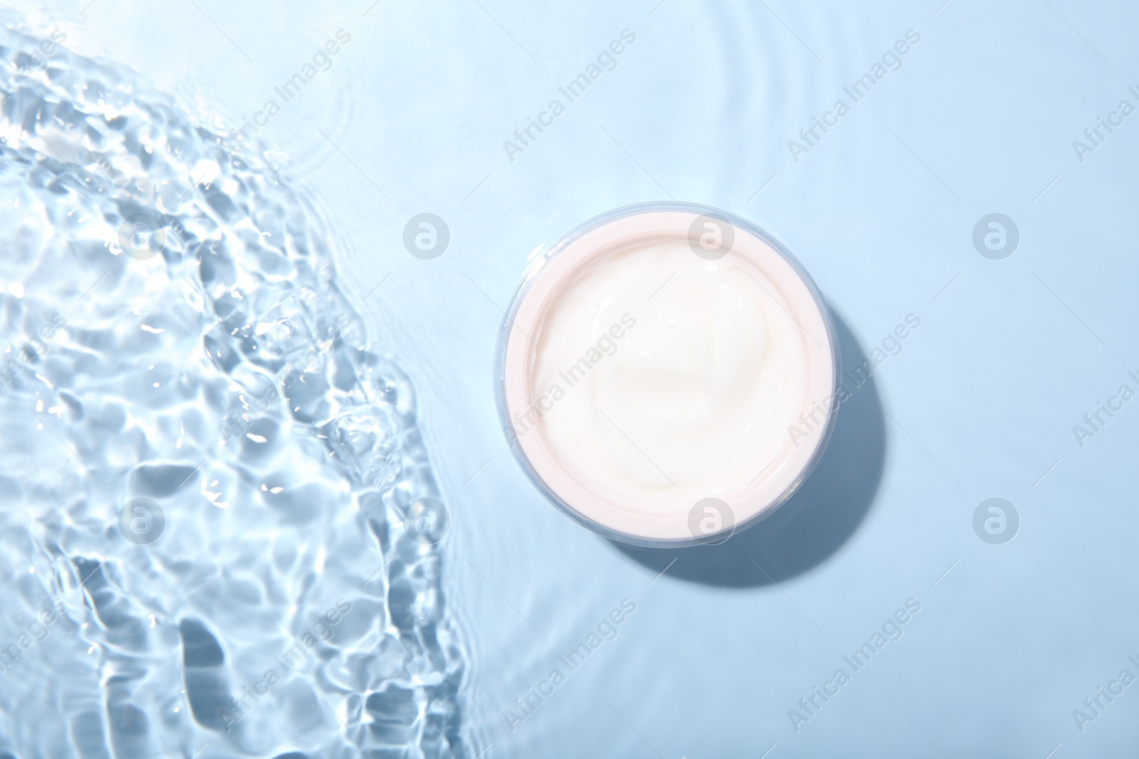 Photo of Cosmetic product. Jar with cream in water on light blue background, top view