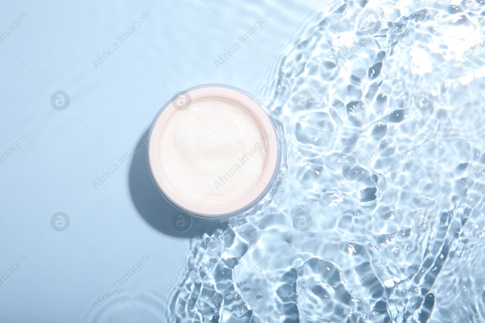 Photo of Cosmetic product. Jar with cream in water on light blue background, top view