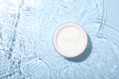 Cosmetic product. Jar with cream in water on light blue background, top view. Space for text