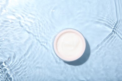 Photo of Cosmetic product. Jar with cream in water on light blue background, top view