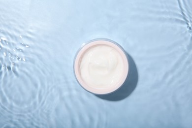 Cosmetic product. Jar with cream in water on light blue background, top view