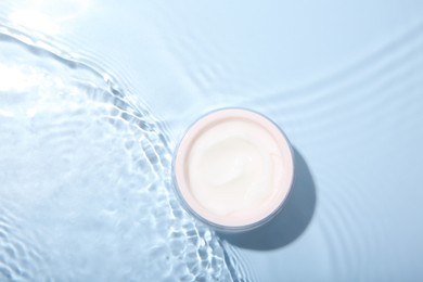 Cosmetic product. Jar with cream in water on light blue background, top view