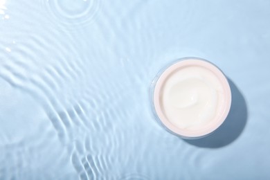 Photo of Cosmetic product. Jar with cream in water on light blue background, top view. Space for text