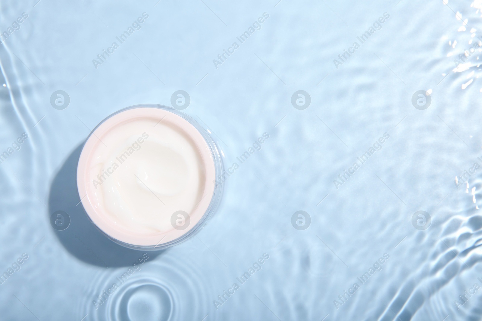 Photo of Cosmetic product. Jar with cream in water on light blue background, top view. Space for text