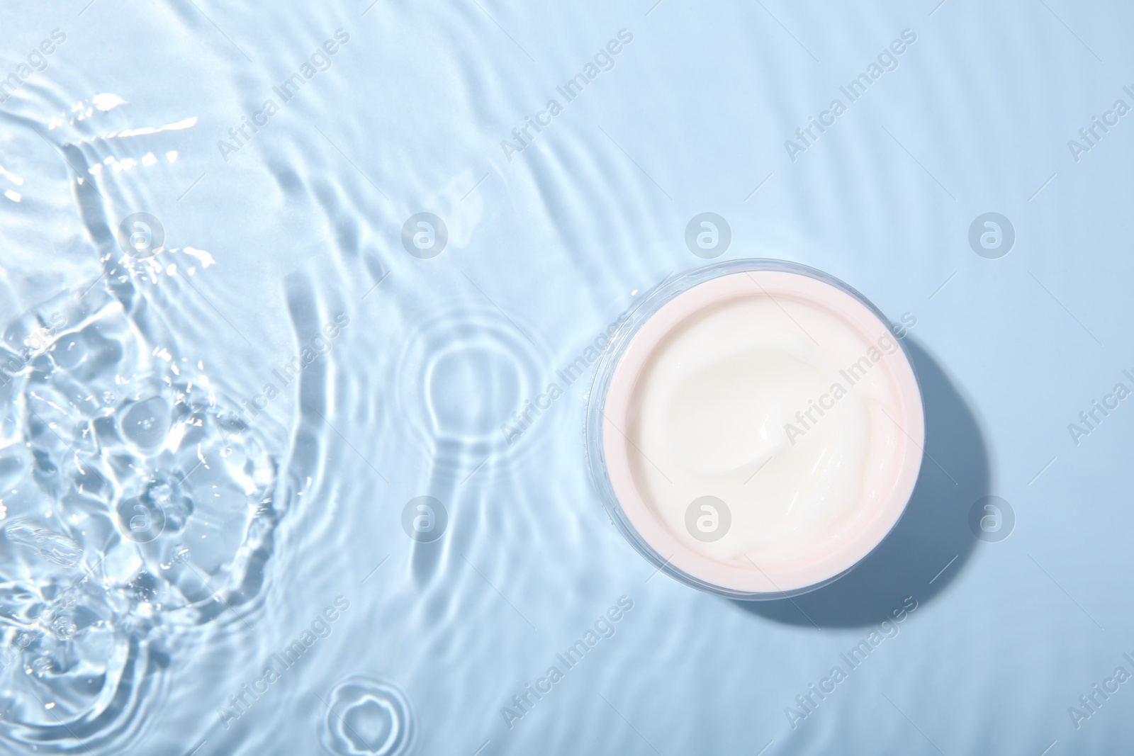 Photo of Cosmetic product. Jar with cream in water on light blue background, top view. Space for text