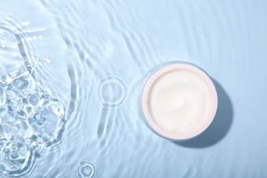 Photo of Cosmetic product. Jar with cream in water on light blue background, top view. Space for text