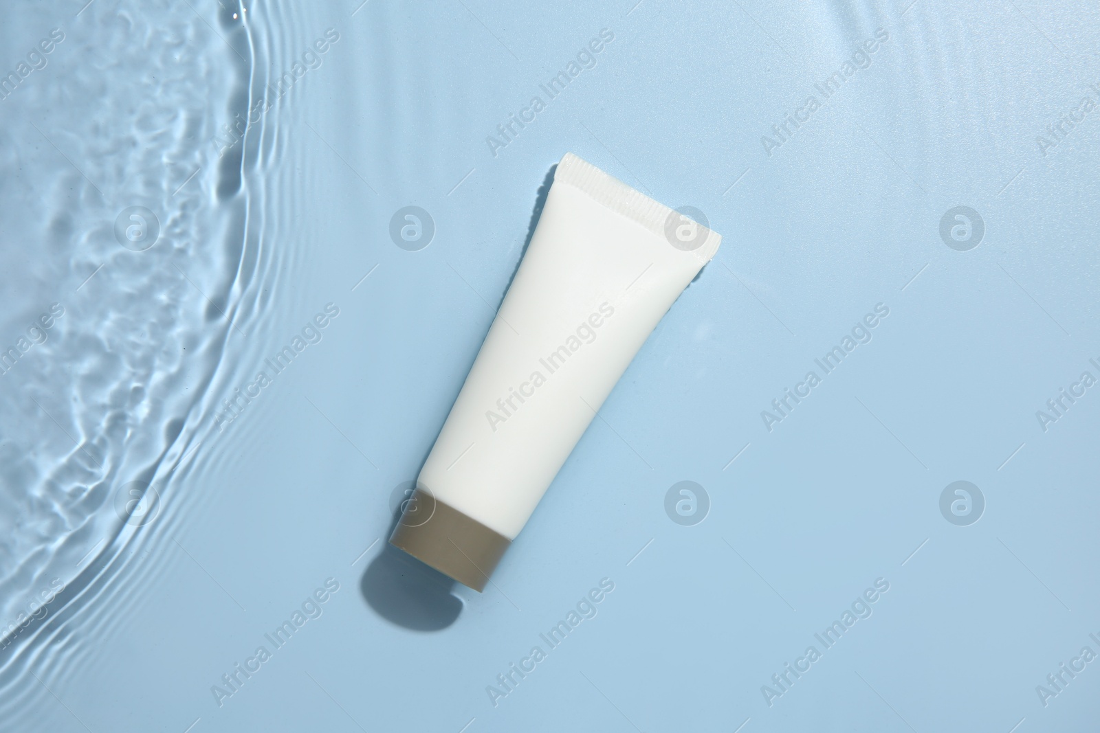 Photo of Cosmetic product. Tube with cream in water on light blue background, top view