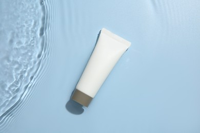 Photo of Cosmetic product. Tube with cream in water on light blue background, top view