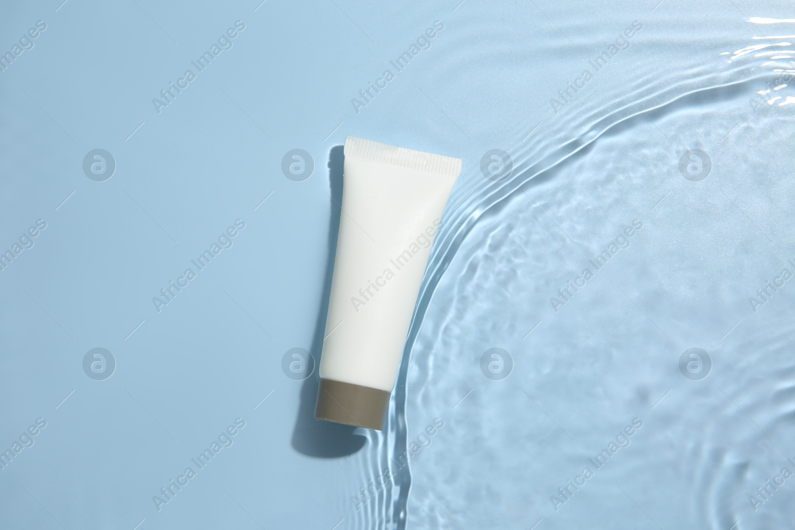 Photo of Cosmetic product. Tube with cream in water on light blue background, top view