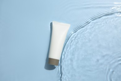 Cosmetic product. Tube with cream in water on light blue background, top view